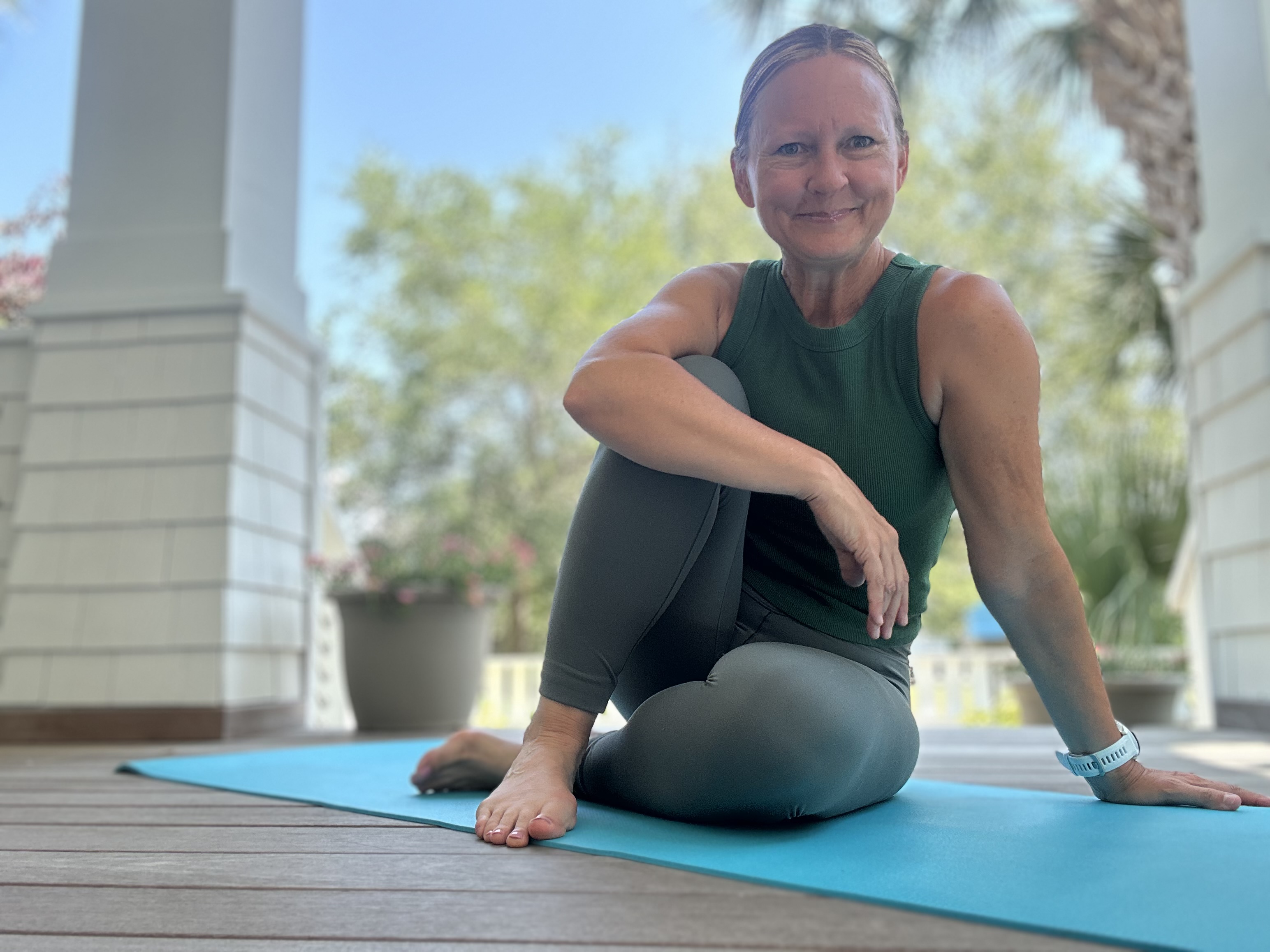 Dana sitting on a yoga mat on a sunny porch, smiling warmly